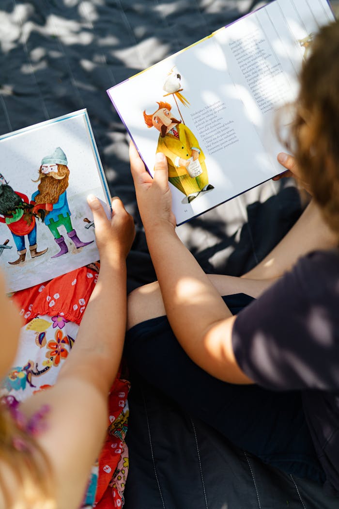Two children enjoying storybooks in a sunny outdoor setting with leaf shadows.