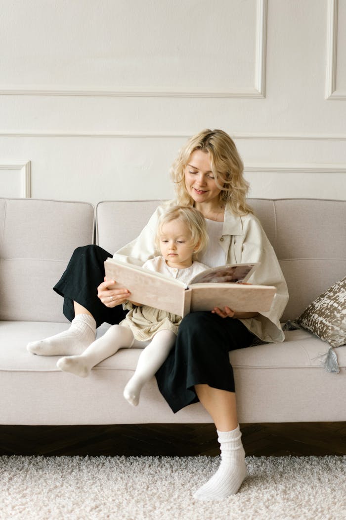 A mother and daughter enjoy storytime on a cozy living room couch.